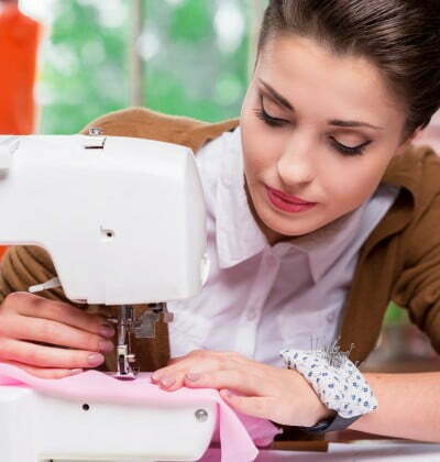Everything should be perfect. Confident female fashion designer working on sewing machine while sitting at her working place